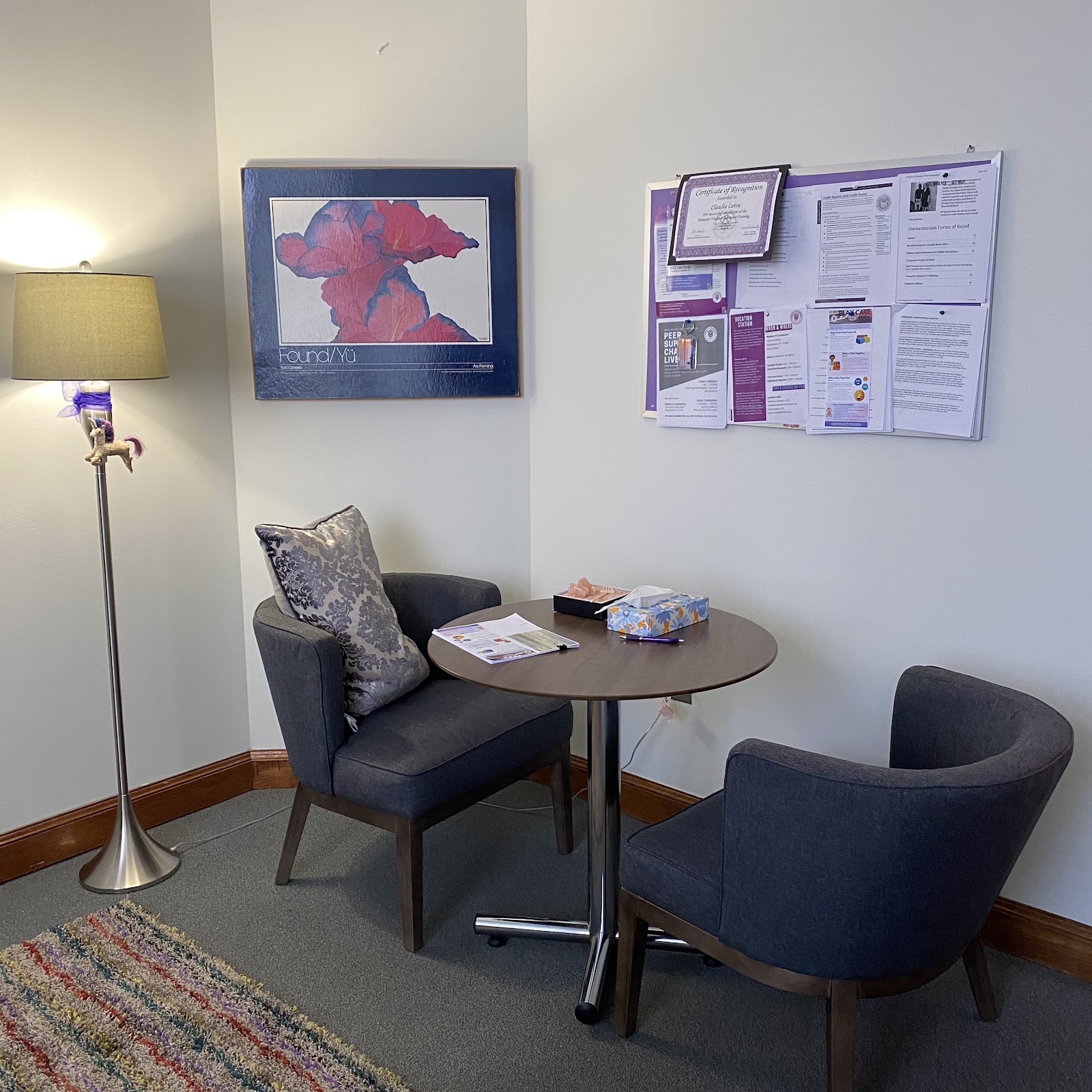 Interior consultation space with dark chairs, round table, floor lamp, and framed artwork on walls