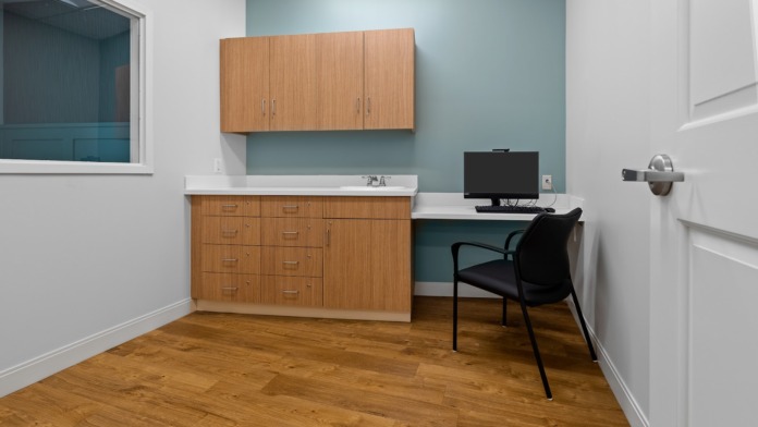 Interior counselor office featuring wooden cabinetry, sink counter, desk with computer monitor, and teal accent wall
