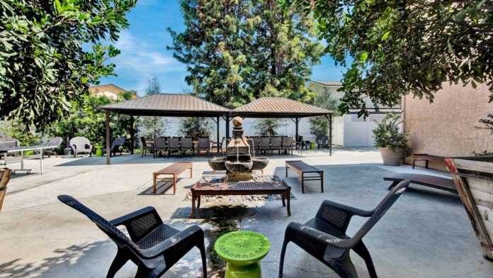 Exterior courtyard featuring covered pavilions, fire pit, lounge seating, and landscaped grounds with mature trees