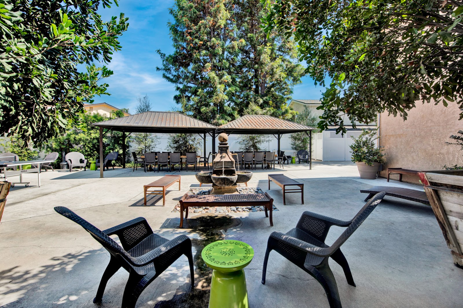 Exterior courtyard featuring covered pavilions, fire pit, lounge seating, and landscaped grounds with mature trees