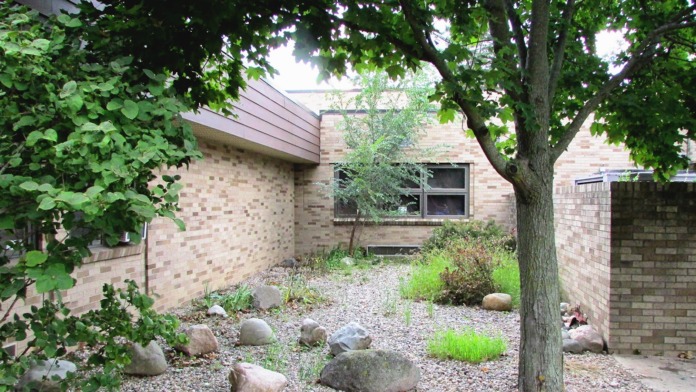 Exterior courtyard area with brick building, mature trees, gravel landscaping, and building windows.