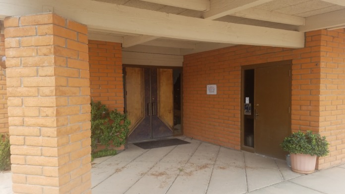 Interior covered entryway with brick columns, wooden doors, ceiling beams, and tiled flooring