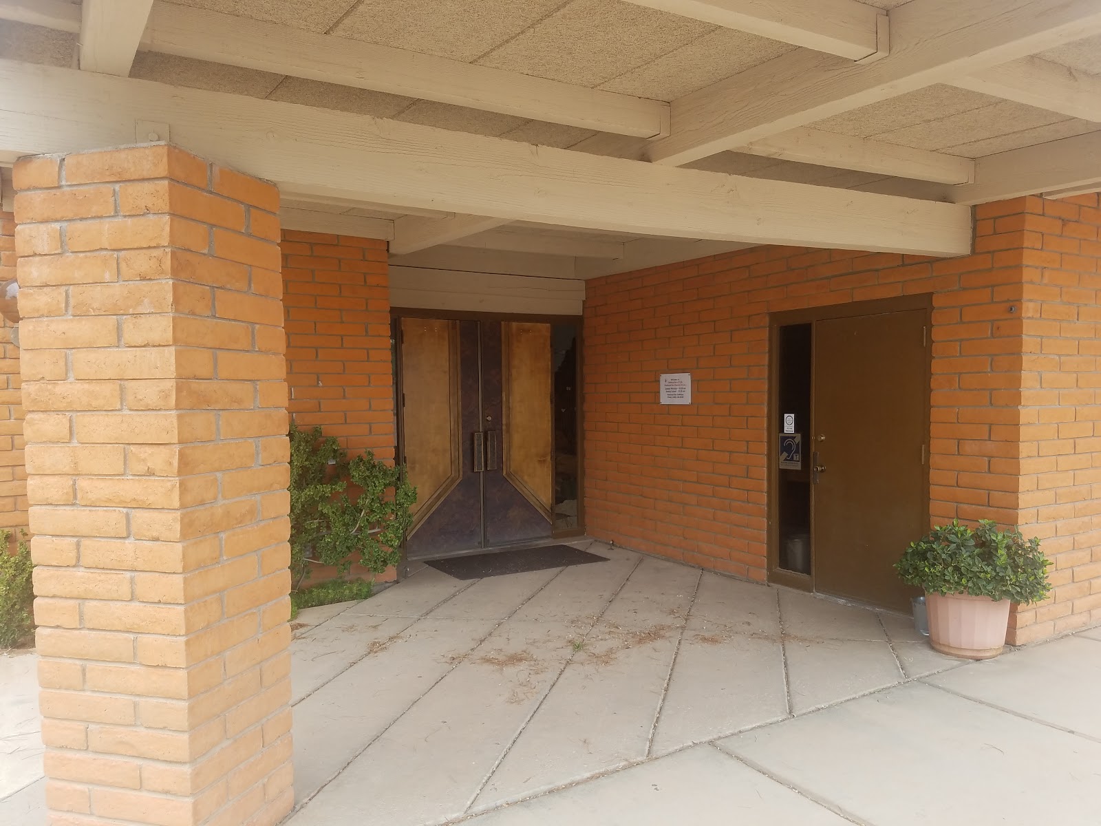 Interior covered entryway with brick columns, wooden doors, ceiling beams, and tiled flooring