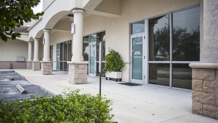 Exterior covered entrance area with stone columns, glass doors, and landscaping with shrubs