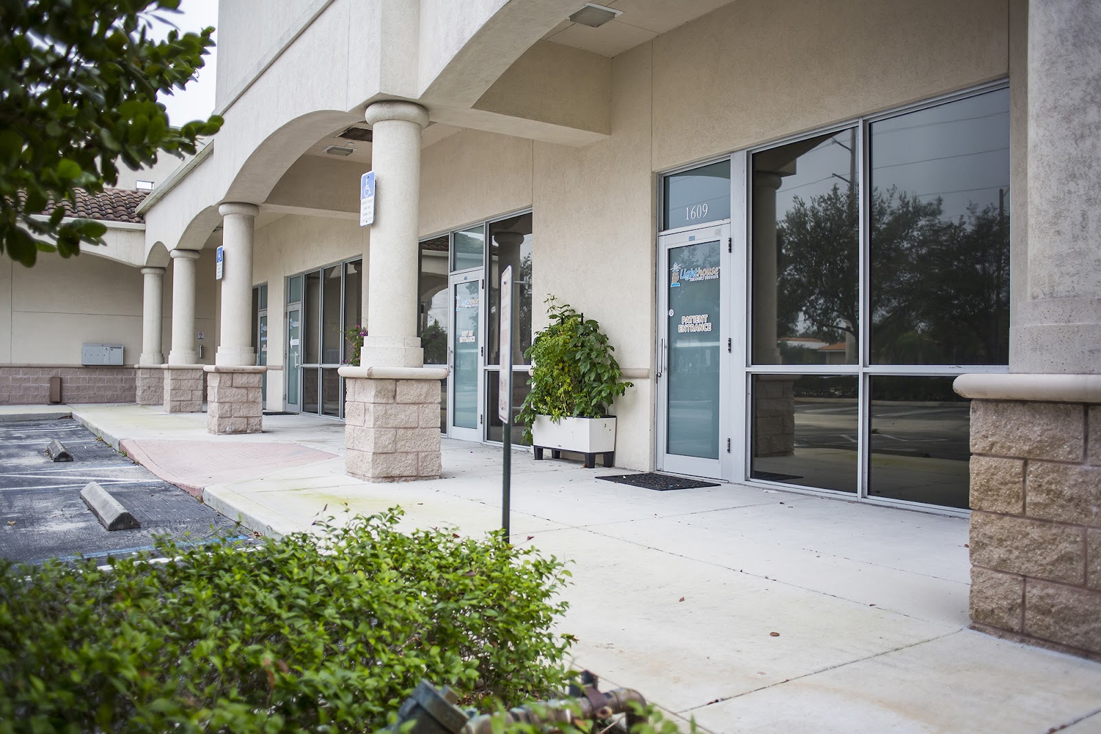 Exterior covered entrance area with stone columns, glass doors, and landscaping with shrubs