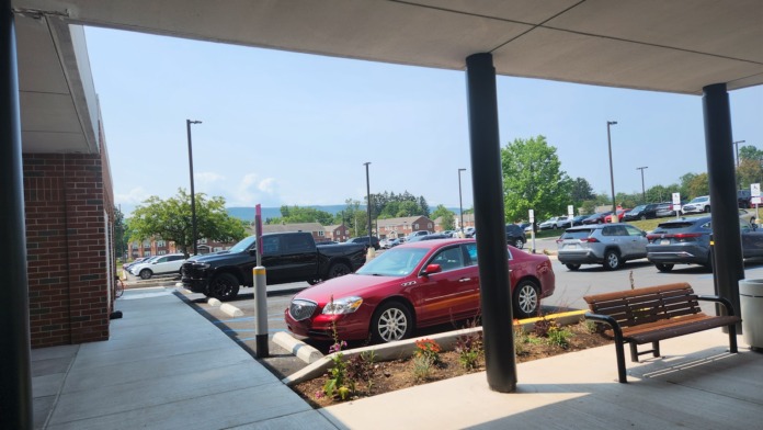 Exterior covered entrance with parking lot view, brick building facade, landscaping and seating bench