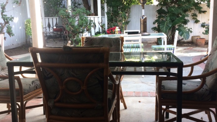 Exterior covered patio with dining furniture, heater, plants, and access to surrounding courtyard space