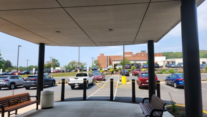 Exterior covered patio with benches, trash receptacle, parking lot and brick building visible in background