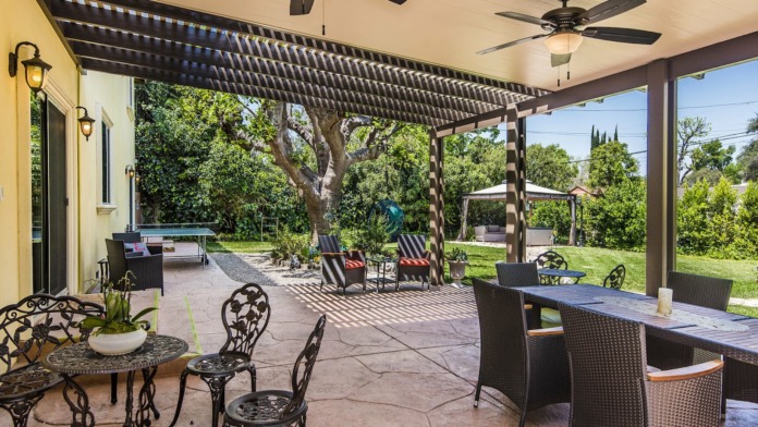 Exterior covered patio with yellow walls, pergola, metal dining furniture, checkered flooring and landscape views