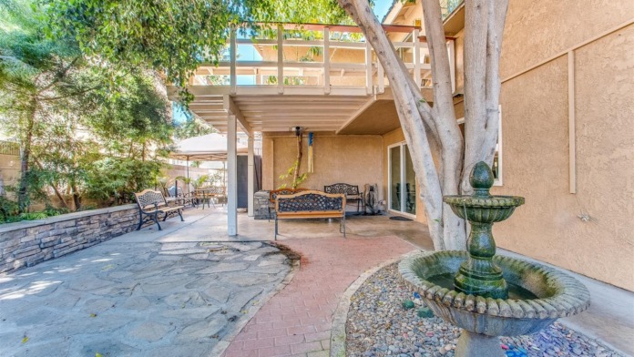Exterior covered patio area with decorative benches, fire pit feature, mature trees, and additional seating pavilion in background