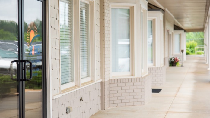 Exterior covered porch area with white trim windows, brick foundation, entrance doors, and landscape plantings