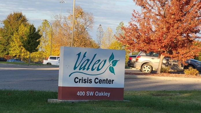 Valeo Crisis Center ground signage with parking area, vehicles, and autumn foliage surrounding the facility