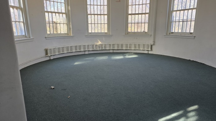 Interior circular room with barred windows, curved walls, natural lighting, and blue-grey flooring.