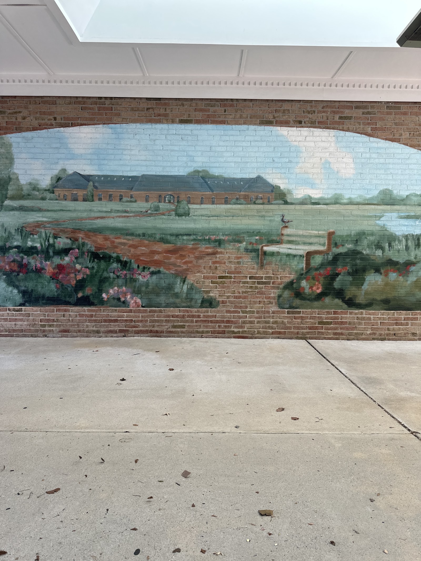 Interior wall mural depicting rural landscape with building, water, and flowering plants in watercolor style
