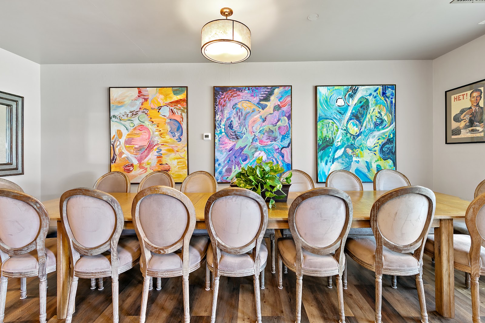 Interior dining space with long wooden table, upholstered chairs, vibrant abstract paintings, and decorative lighting