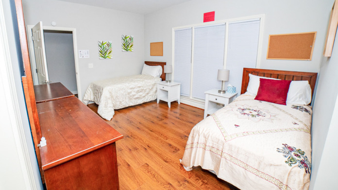 Interior bedroom with two twin beds with white linens, wooden desk, nightstands, and window with blinds for privacy