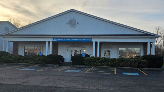 Exterior facility facade at dusk showing columned entrance, parking spaces, and landscaping