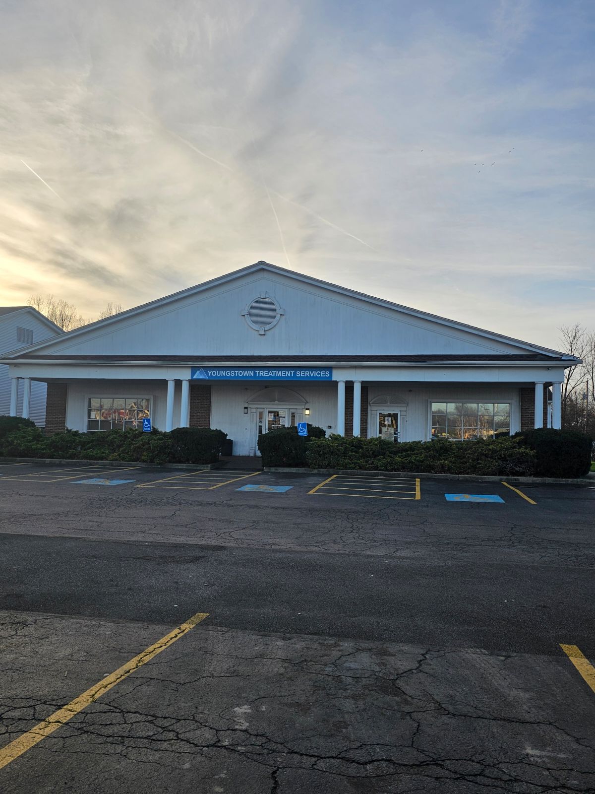 Exterior facility facade at dusk showing columned entrance, parking spaces, and landscaping
