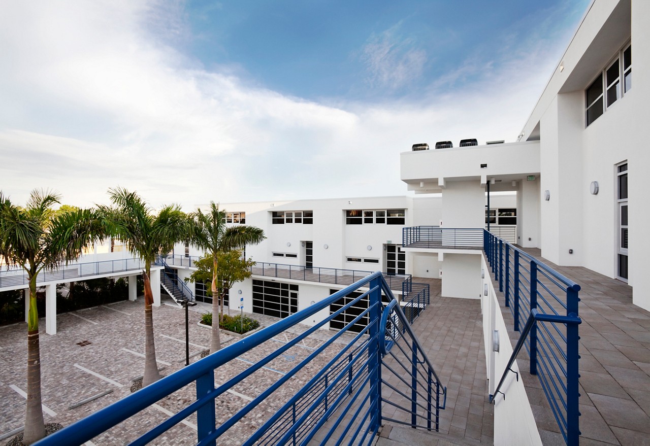 Exterior elevated deck area with blue metal railings overlooking paved courtyard and facility building.