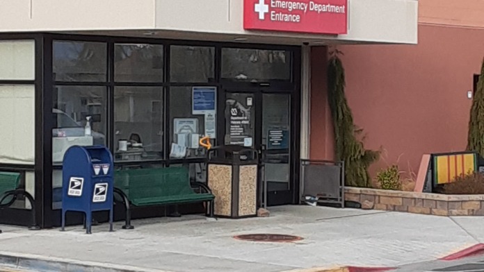 Exterior Emergency Department entrance with red and white signage, glass doors, mailbox, bench seating, and red-brown facade