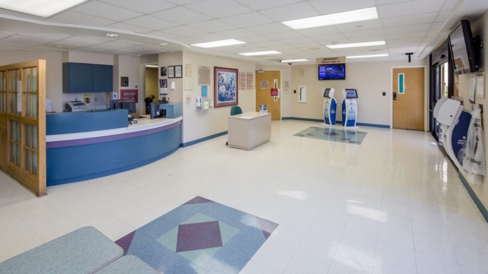 Interior emergency department lobby with blue reception desk, seating area, and information displays