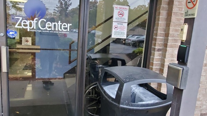 Exterior entrance vestibule showing glass doors with Zepf Center logo, no-smoking signage, covered overhang, and trash receptacle with flowering plants