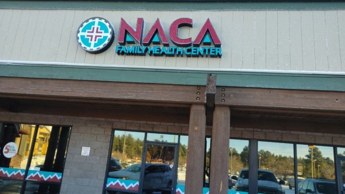 Exterior view of NACA Family Health Center entrance covered in light snow with parking area and facility signage