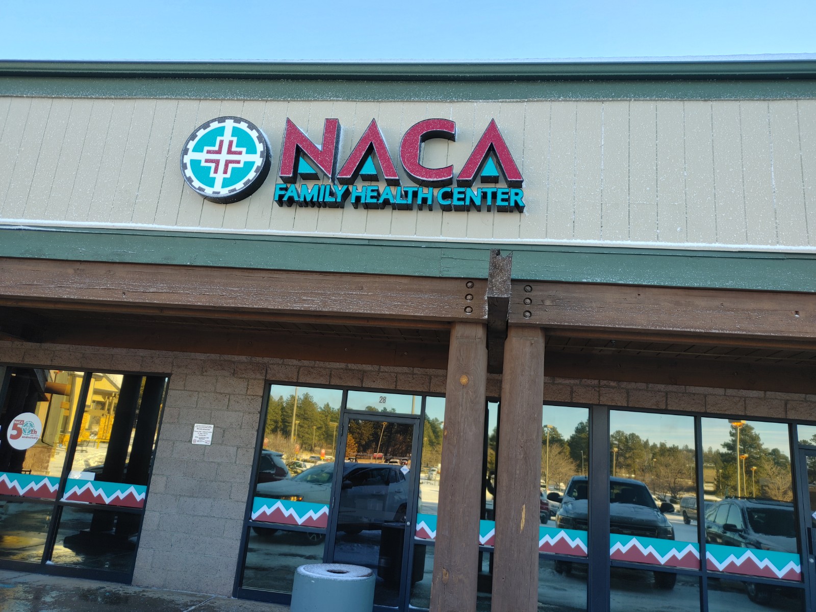 Exterior view of NACA Family Health Center entrance covered in light snow with parking area and facility signage