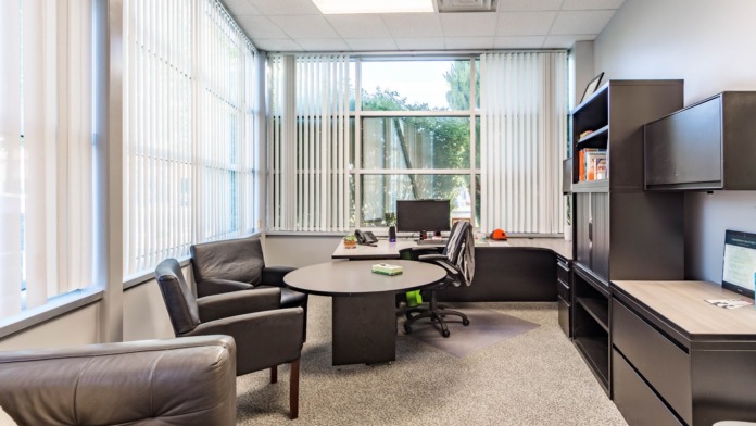 Interior executive office with black leather chairs, round table, desk area, windows with vertical blinds, and natural lighting