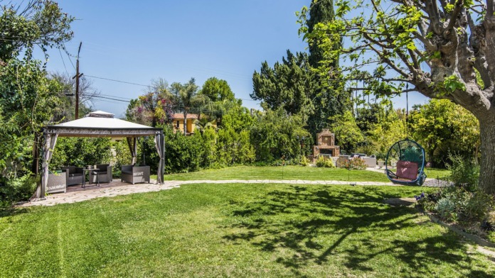 Outdoor landscape with manicured lawn, mature shade trees, pergola seating structure and garden beds