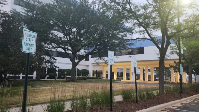 Exterior view showing facility grounds with trees, landscaping, and parking area with directional signage