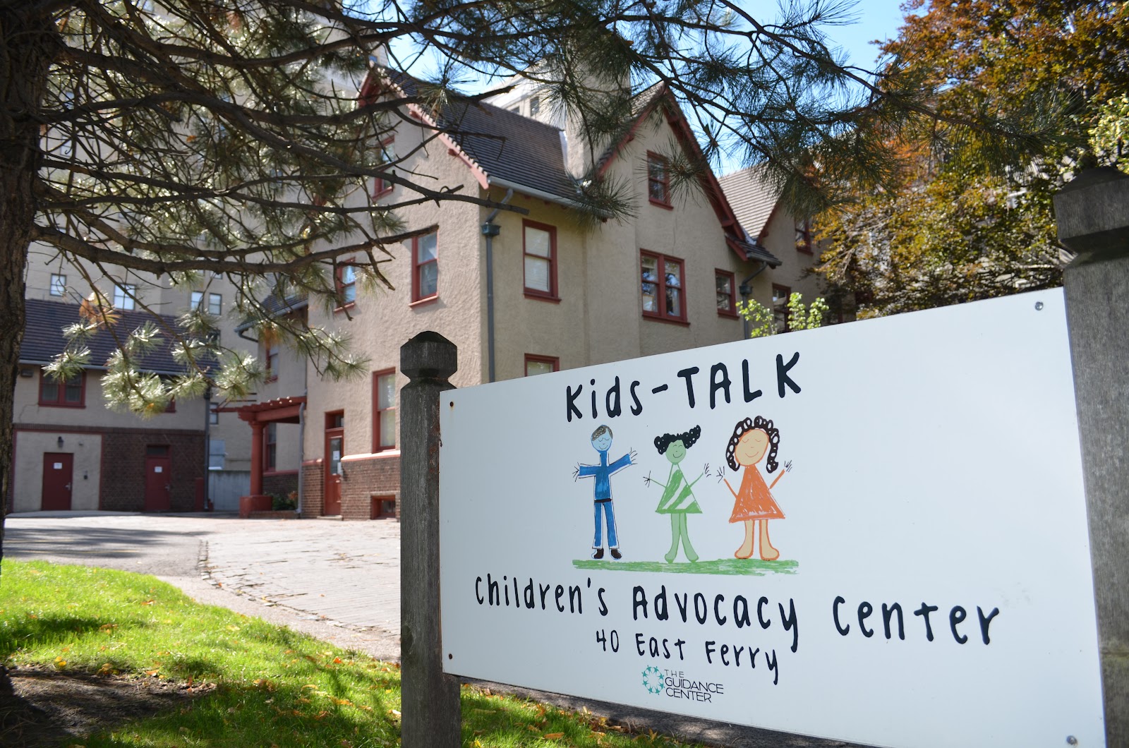 Outdoor view showing Kids-TALK Children's Advocacy Center sign with illustrated children, building exterior, and landscaped grounds