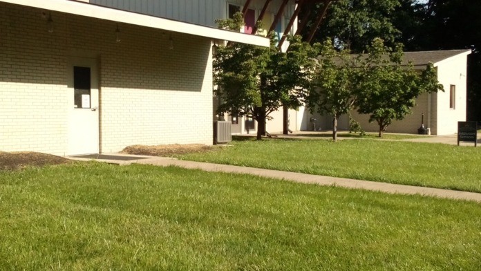 Exterior view of treatment center with modern architecture, green lawn, tree canopy, and covered outdoor structure