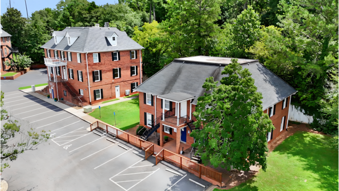 Exterior aerial view showing brick buildings, parking lot, green lawn areas, and surrounding trees