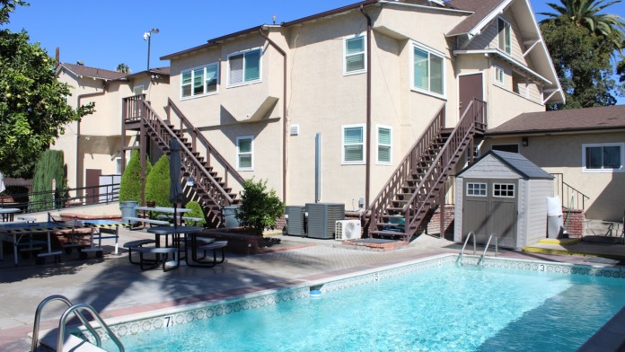 Exterior courtyard view showing multi-story residential building with external staircases, picnic tables, and swimming pool amenity