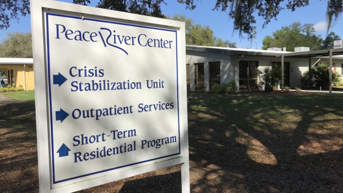 Exterior facility sign for Peace River Center Crisis Stabilization Unit with campus buildings and landscaping visible in background