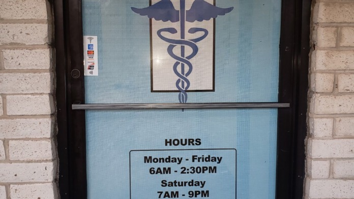 Exterior entrance door with glass panel displaying facility name, medical caduceus logo, and operating hours information