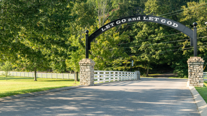 Exterior showing main entrance gate with Let Go and Let God text, white fence, and tree-lined driveway