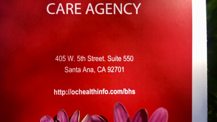 Exterior signage displaying OC Health Care Agency logo, address, and contact information with decorative flowers