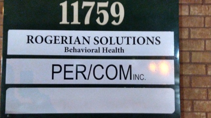 Exterior building sign showing address 11759 with Rogerian Solutions Behavioral Health and PER/COM Inc. names on brick wall