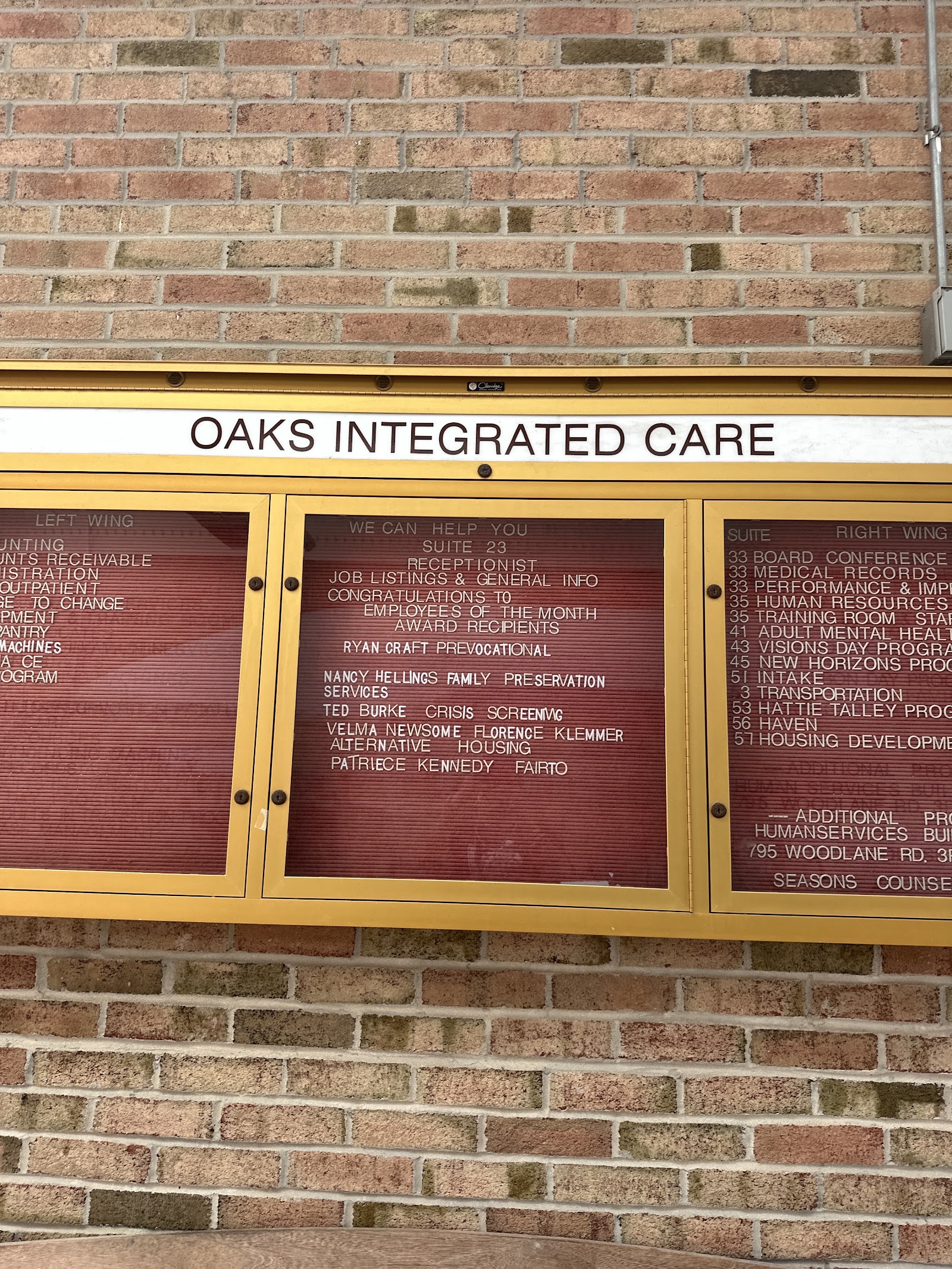 Interior entryway bulletin board mounted on brick wall with facility name and service directory information