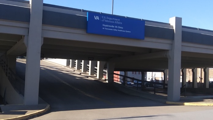 Exterior entrance showing blue VA signage and clinic access under roadway overpass structure