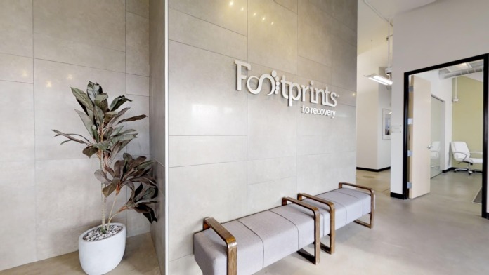 Interior entrance hallway with Footprints to Recovery signage, seating benches, plants, and glass doors