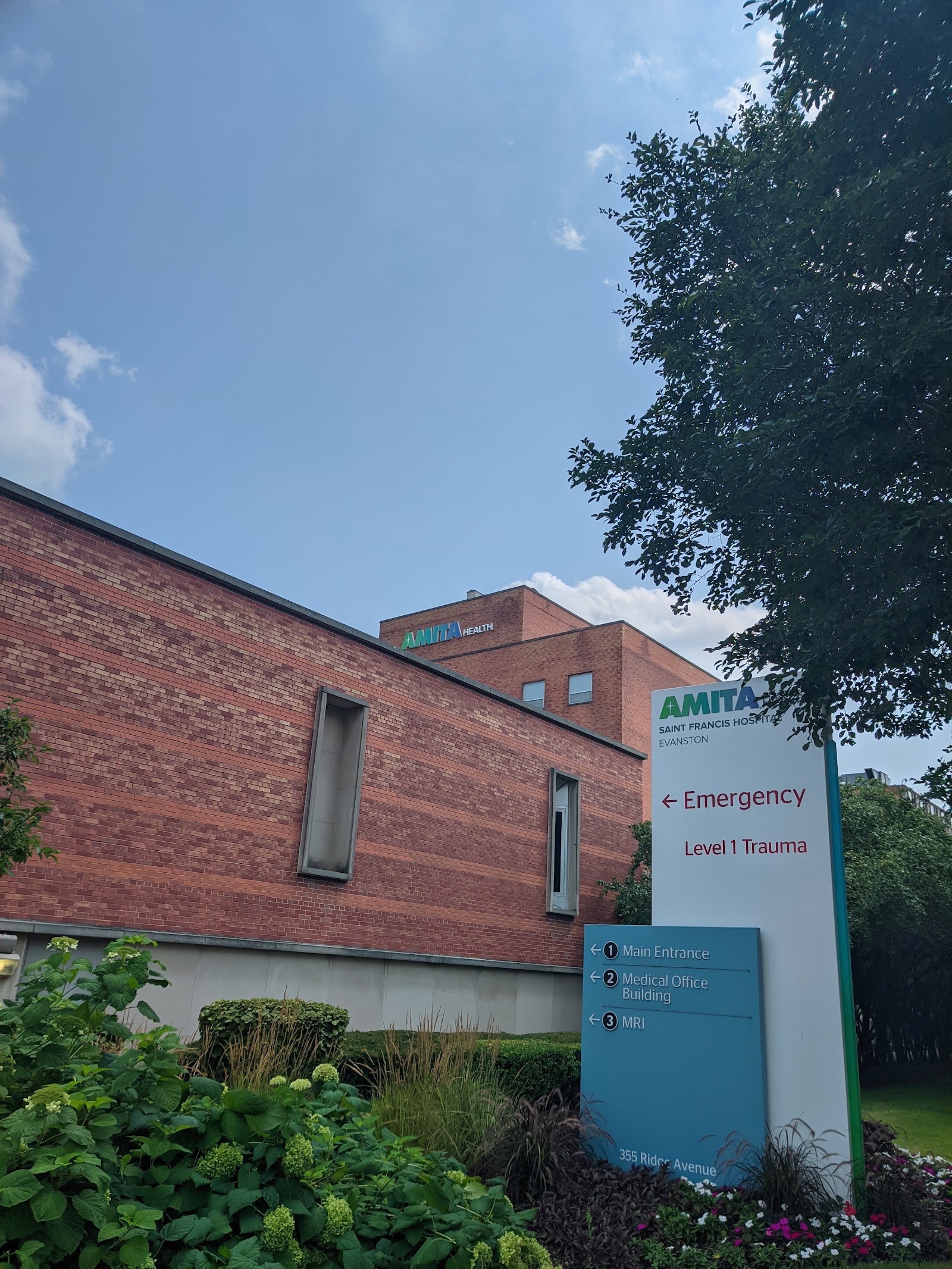 Exterior showing medical office building entrance with emergency and location signage, brick construction, and landscaping