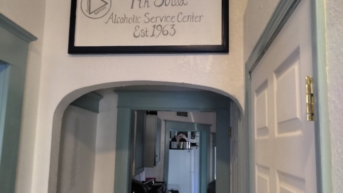 Interior hallway with welcome signage for Alcoholic Service Center established 1963, white walls, and archway.