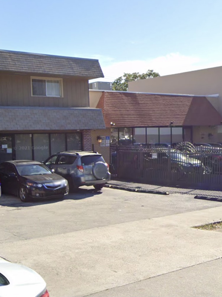 Exterior building showing brick treatment facility with tan metal siding, windows, parking area, vehicles, and accessibility ramp.