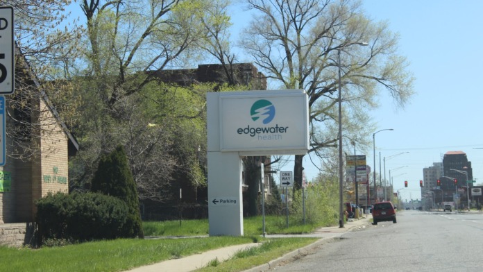 Exterior side view of Edgewater Health facility showing concrete facade, trees, and street frontage on West 6th Avenue