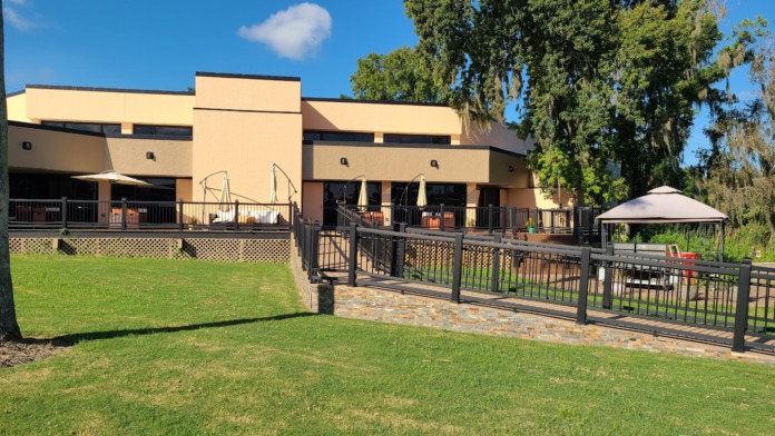 Exterior facility building with manicured lawn, wooden deck railing, and tree-lined property