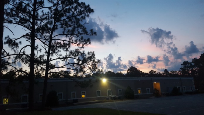 Exterior view of treatment facility building with windows lit at twilight, pine trees in background