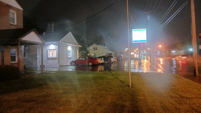 Nighttime exterior view of facility buildings, parking lot, street signage, and landscaping in wet conditions